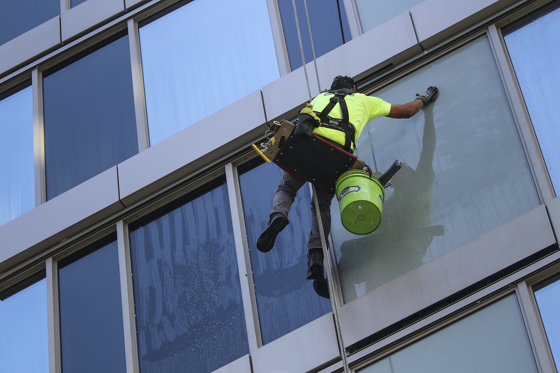 Fassadenreiniger seilt sich an einer Glasfassade ab und zieht eine Scheibe ab
